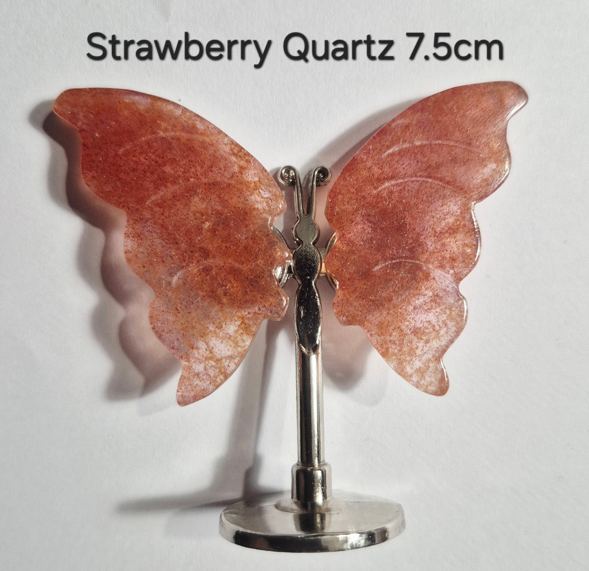 A butterfly-shaped piece made of translucent strawberry quartz with a silver-tone metal stand, shown against a plain white background with the text 'Strawberry Quartz 7.5cm' at the top.