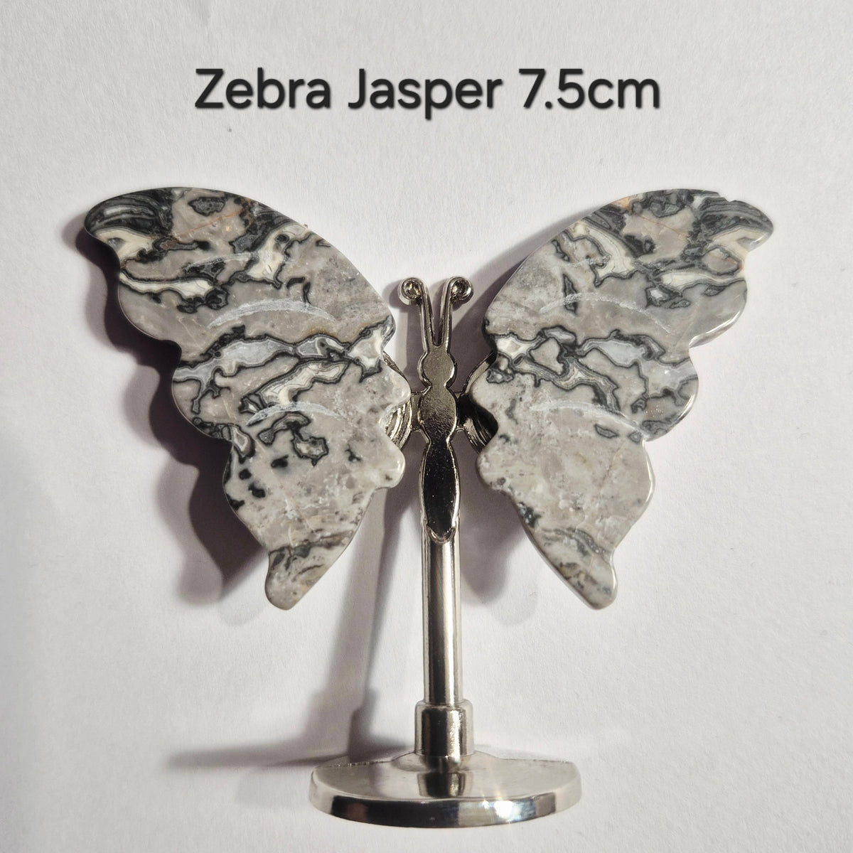 A butterfly-shaped ornament made from zebra jasper with gray and white marbled wings on a silver-tone stand, shown against a plain white background with the text 'Zebra Jasper 7.5cm' above it.