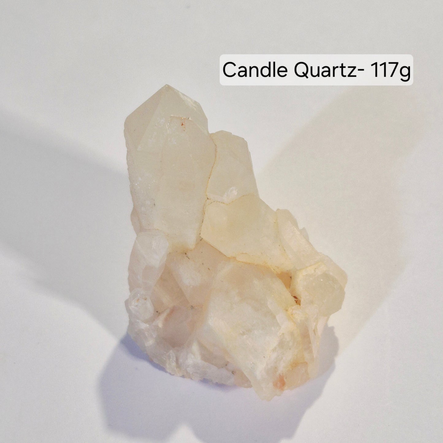 A raw crystal cluster of Candle Quartz, approximately 117g, displayed on a white surface with a soft shadow. The text label 'Candle Quartz- 117g' is positioned in the upper right.
