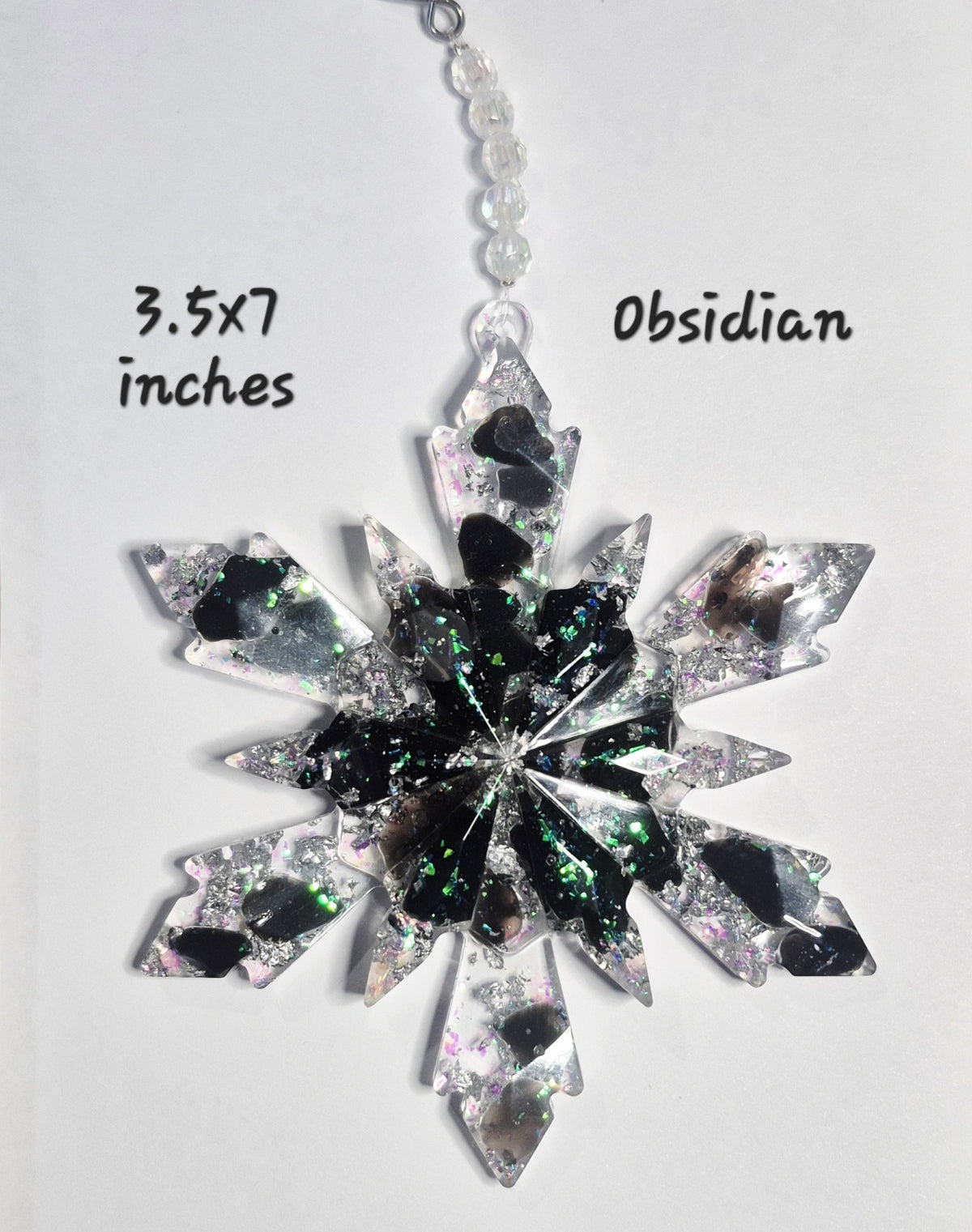 A handmade snowflake ornament made from clear obsidian with black and green glitter, shown on a plain white background with text indicating its size as 3.5x7 inches and the material as Obsidian.