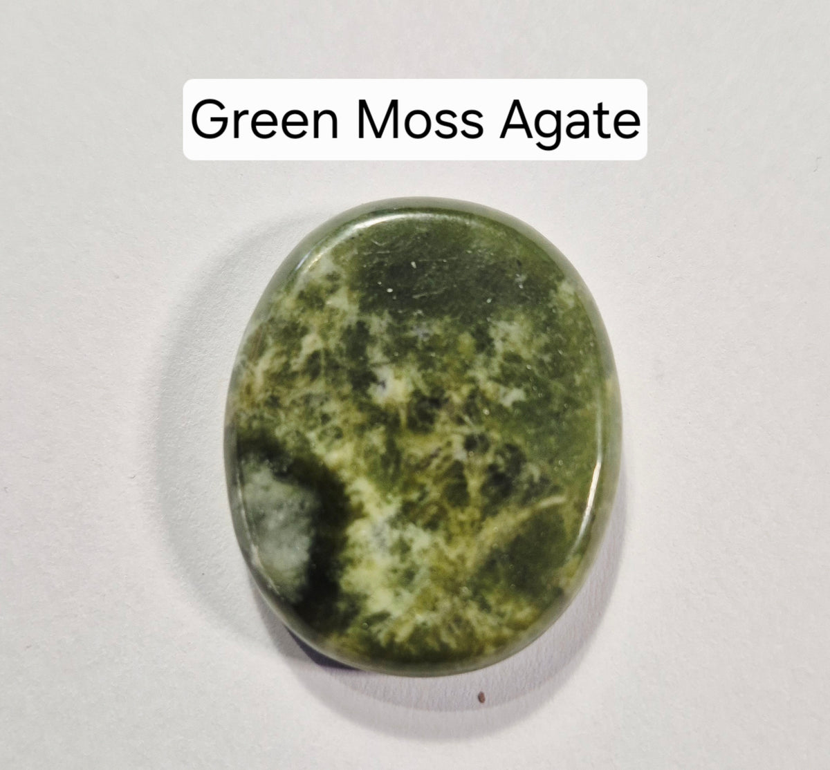 A polished green moss agate worry stone with natural marbled patterns of olive green, dark forest green, and cream, displayed on a light gray background with a text label reading 'Green Moss Agate'.
