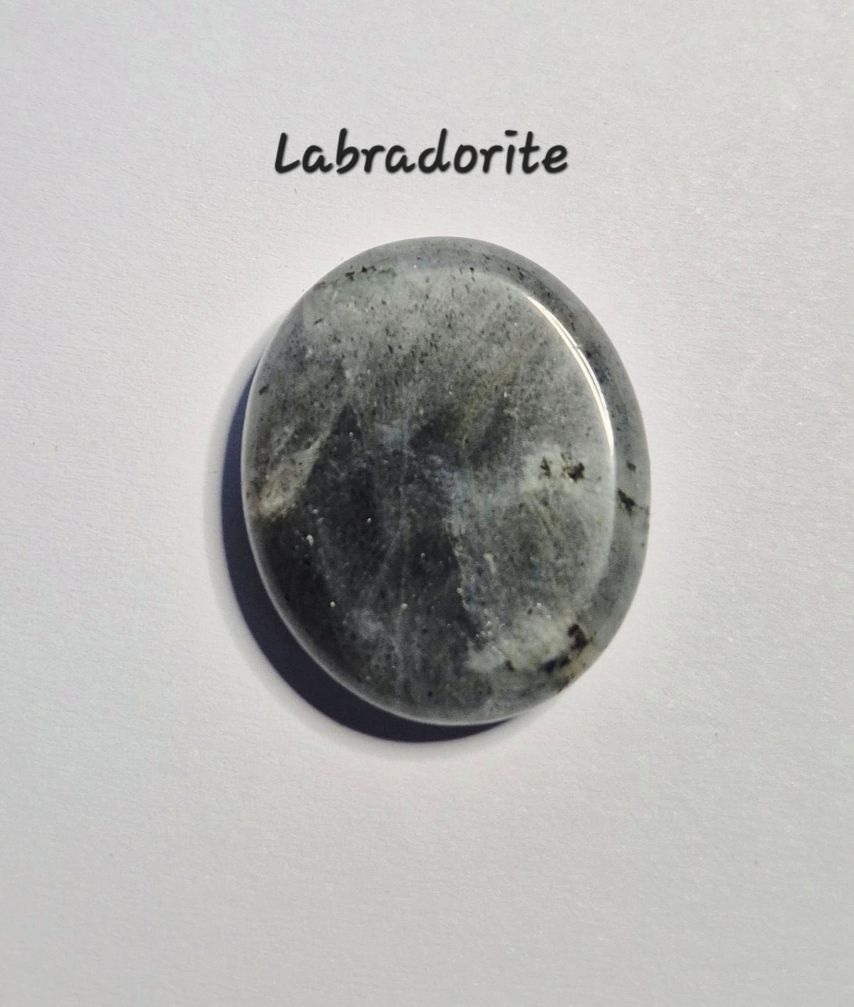 A polished oval labradorite worry stone  with natural gray, black, and white marbling, displayed on a light gray background with the text 'Labradorite' above it.