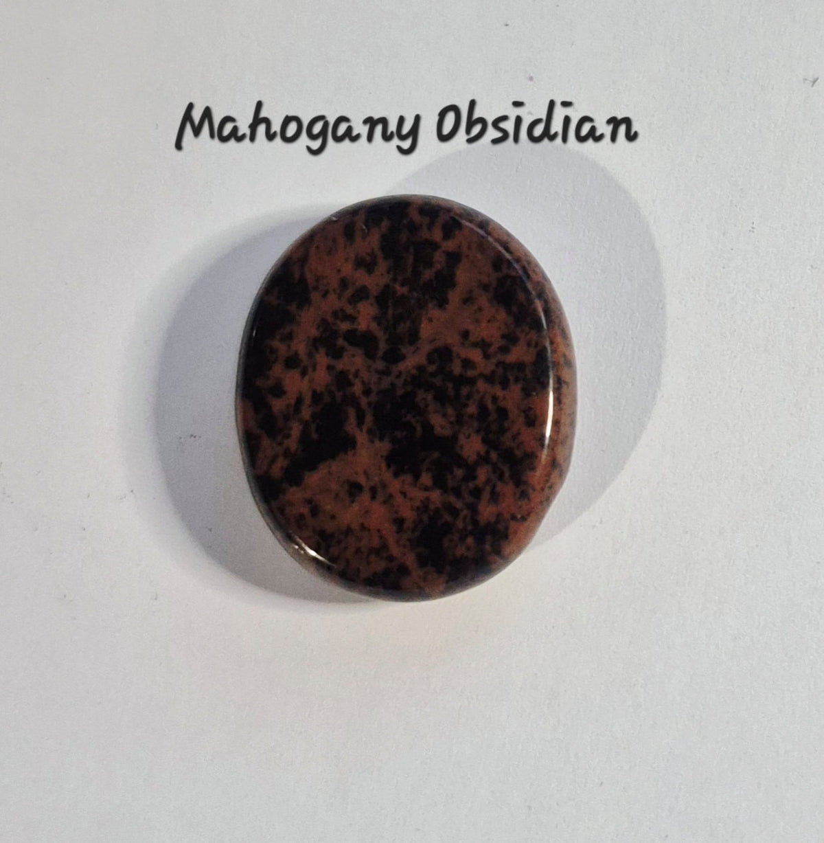 A polished oval worry stone of mahogany obsidian with a mottled dark brown and black pattern, displayed on a white background with the text 'Mahogany Obsidian' above it.