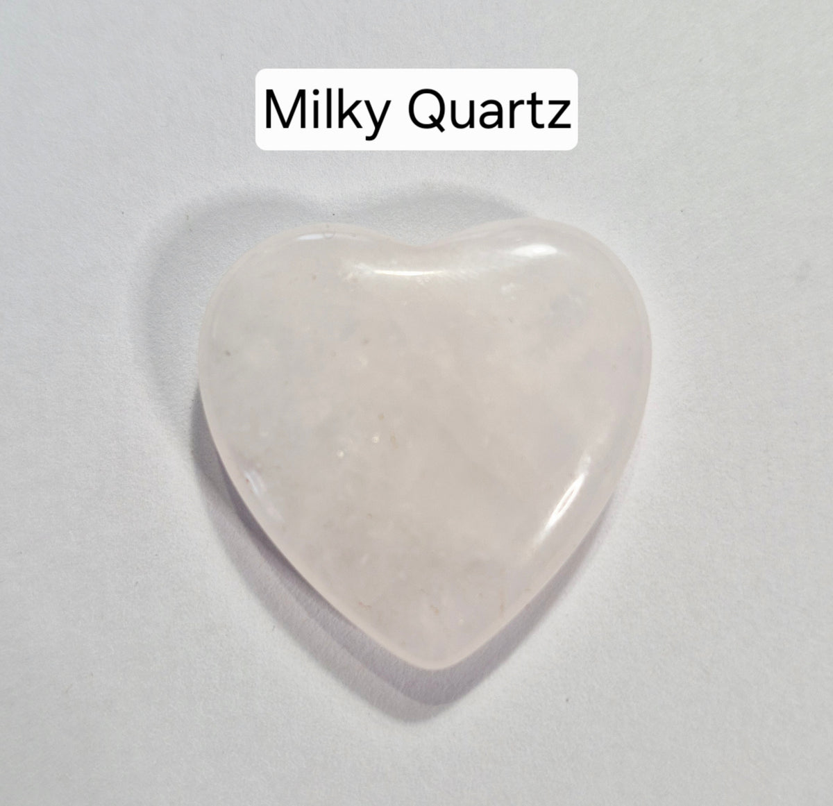 A heart-shaped polished stone labeled 'Milky Quartz' on a plain light background.