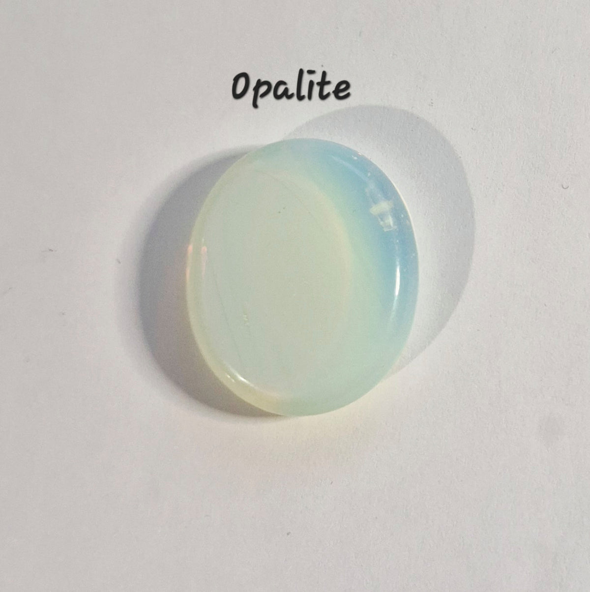 A single oval worry stone with a milky white body and soft pale blue iridescent edges, photographed on a plain white background with the word 'Opalite' written above it.