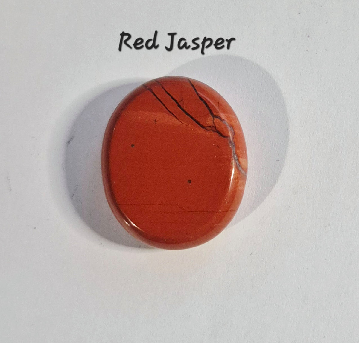 A polished oval red jasper worry stone with natural dark veining, labeled 'Red Jasper' on a white background.