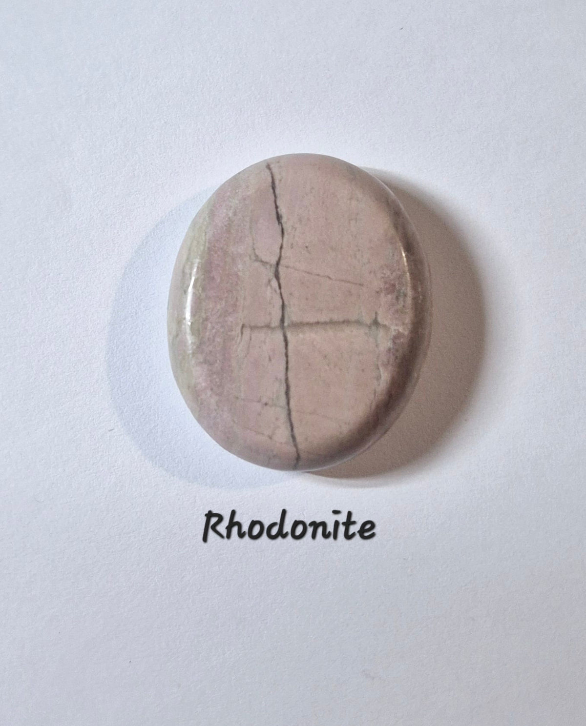A polished oval-shaped rhodonite worry stone  with a dusty pinkish-gray color and natural crack lines, displayed on a white background with the text 'Rhodonite' underneath.
