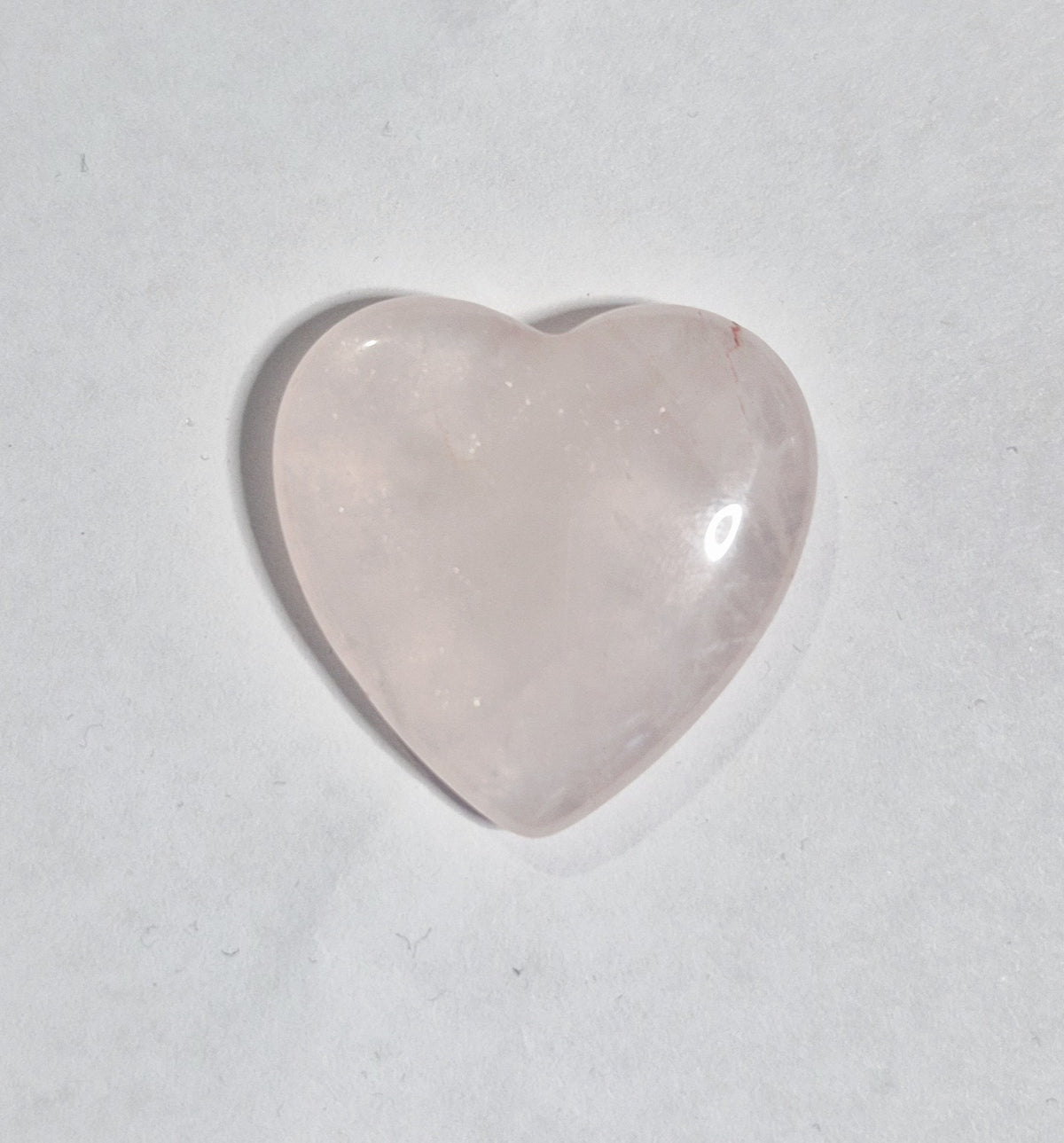 A heart-shaped rose quartz worry stone with a smooth, polished surface, displayed on a neutral light gray background.