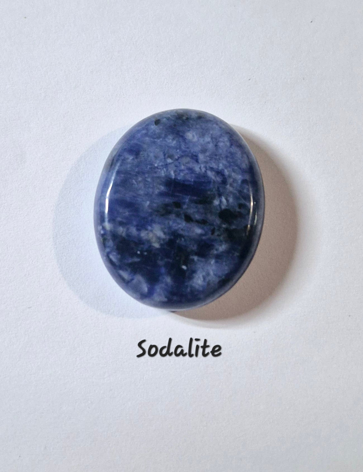 A polished oval worry stone of sodalite gemstone in shades of blue and white, displayed on a white background with the text 'Sodalite' written below.