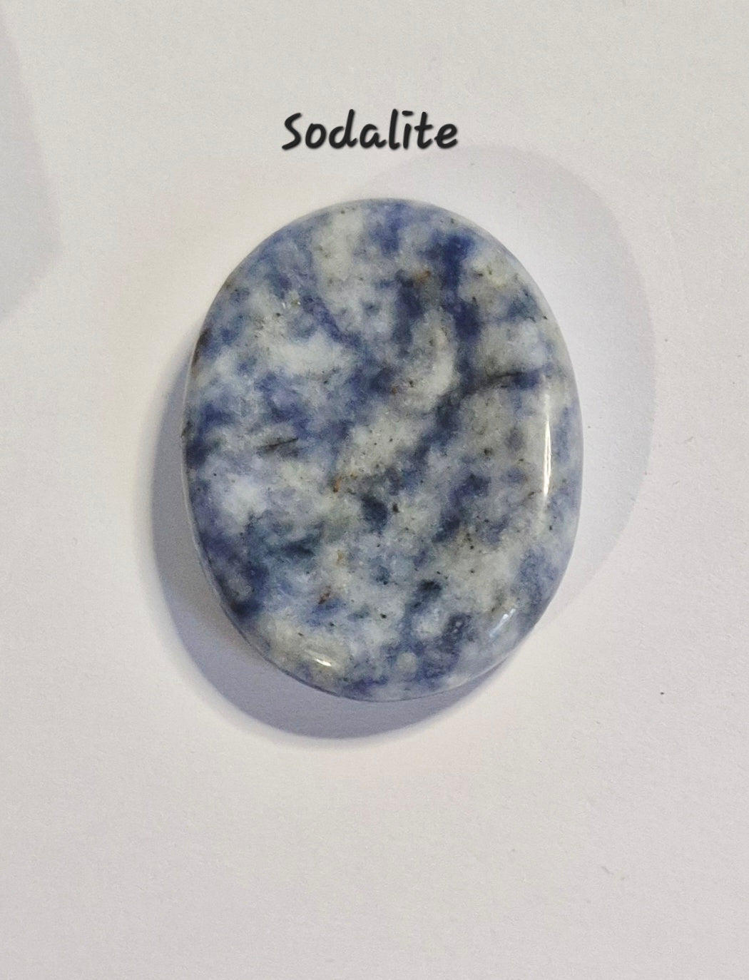 A polished oval cworry stone of sodalite gemstone with a marbled blue and white pattern, displayed on a white background with the text 'Sodalite' written above it.