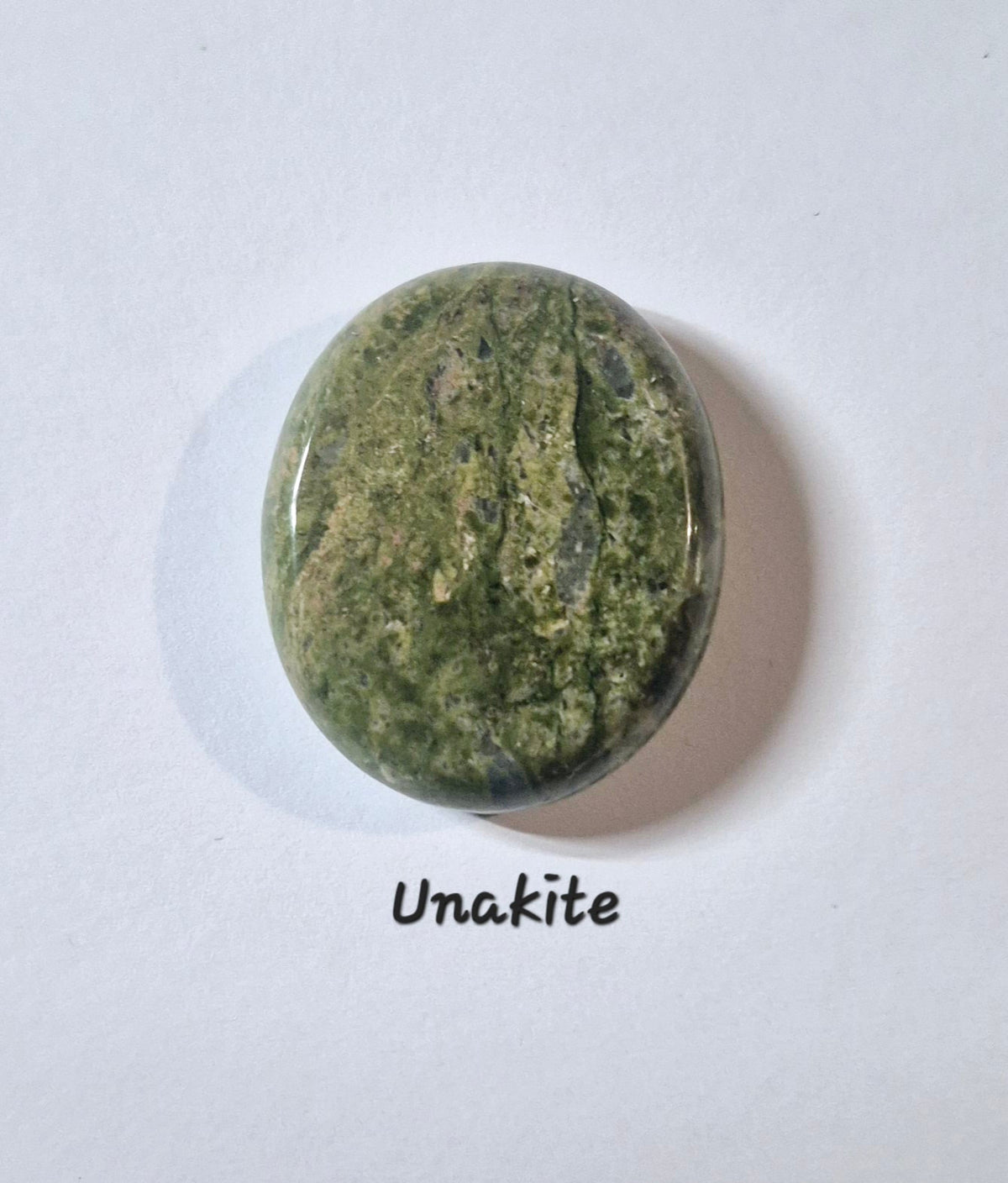 A polished oval worry stone of Unakite gemstone in black text below it, set against a plain white background.