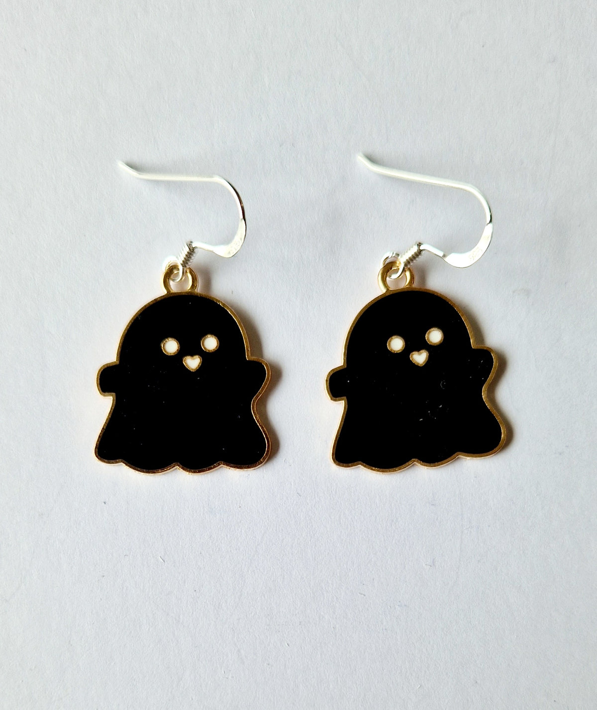 A pair of ghost-shaped drop earrings with black enamel bodies, gold-tone outlines, and sterling silver hooks on a plain white background.