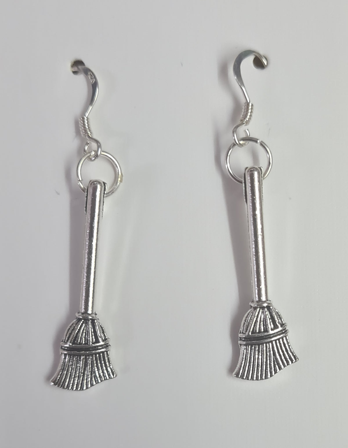 A pair of Sterling Silver witch broomstick dangle earrings with hook backs, displayed against a plain light gray background