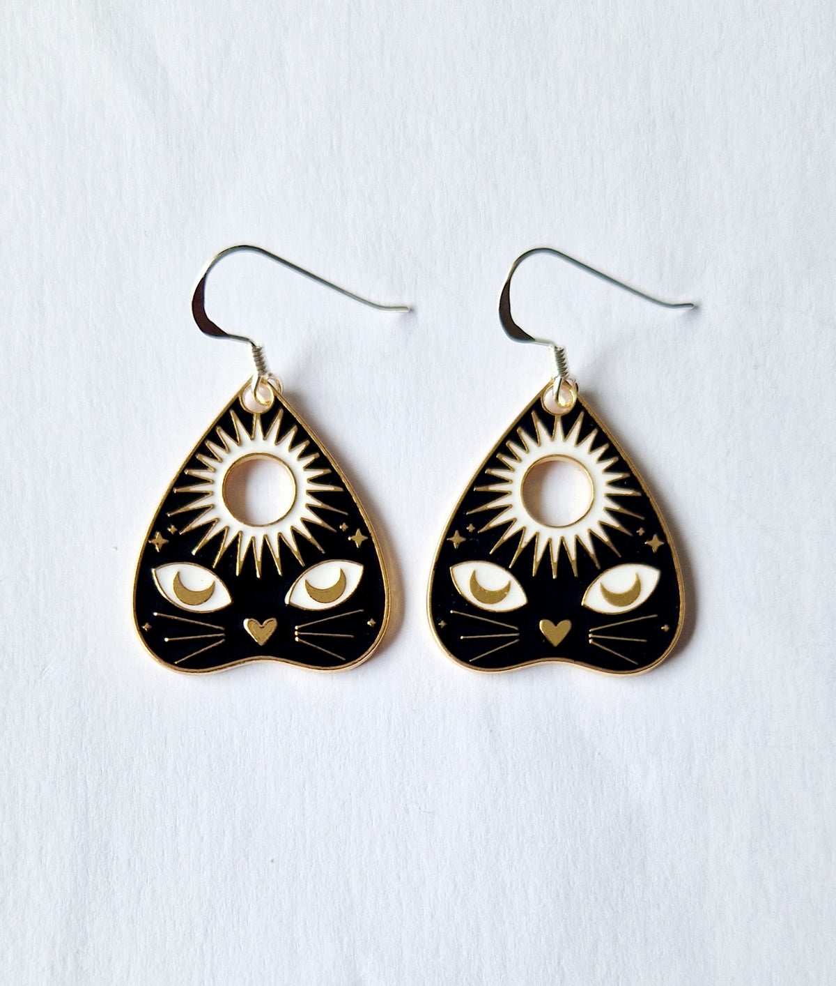 A pair of black and gold teardrop-shaped dangle earrings with a cat face design, shown on a textured white background.