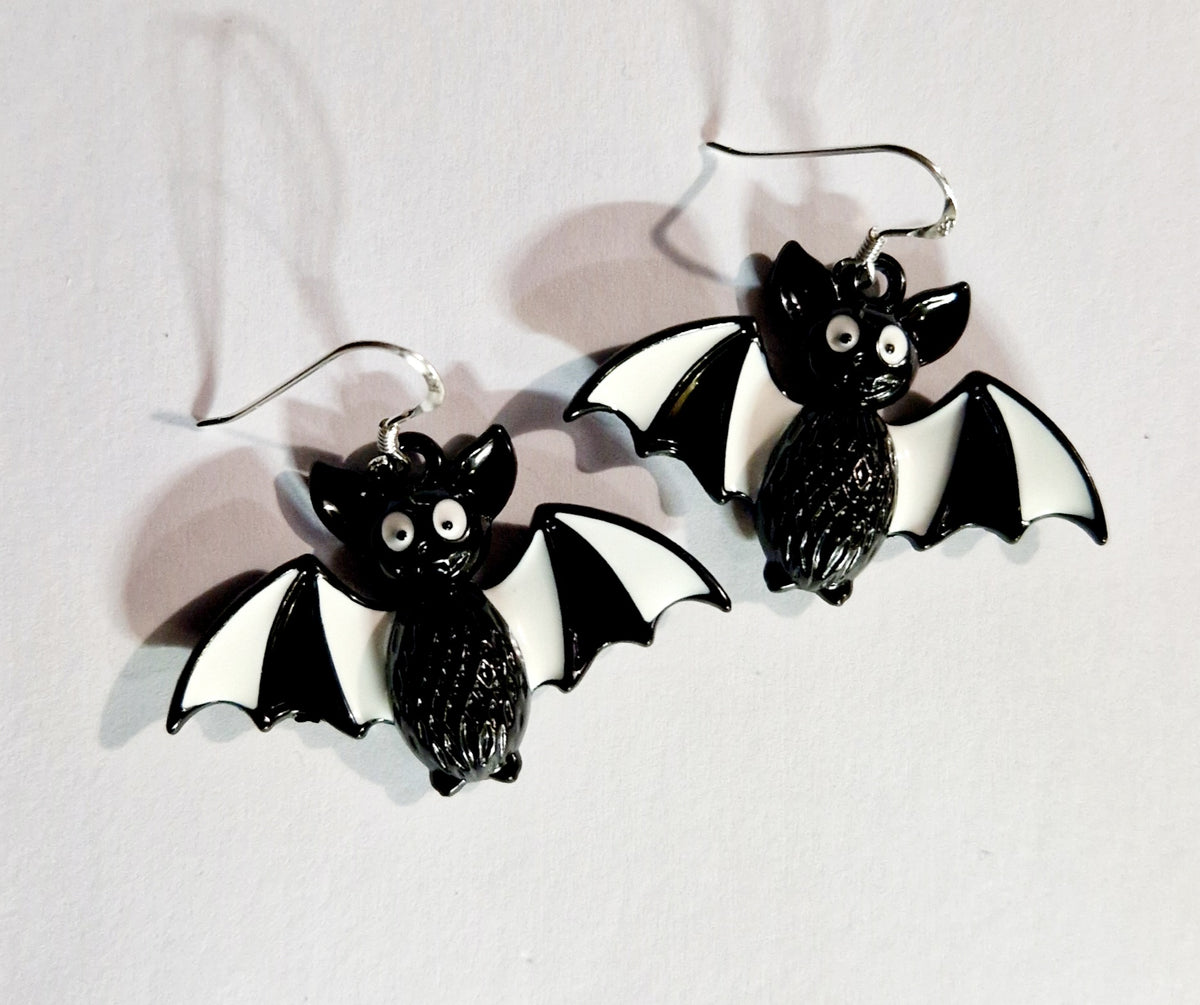 A pair of black and white bat-shaped dangle earrings with sterling silver fishhook wires, displayed on a plain white background.