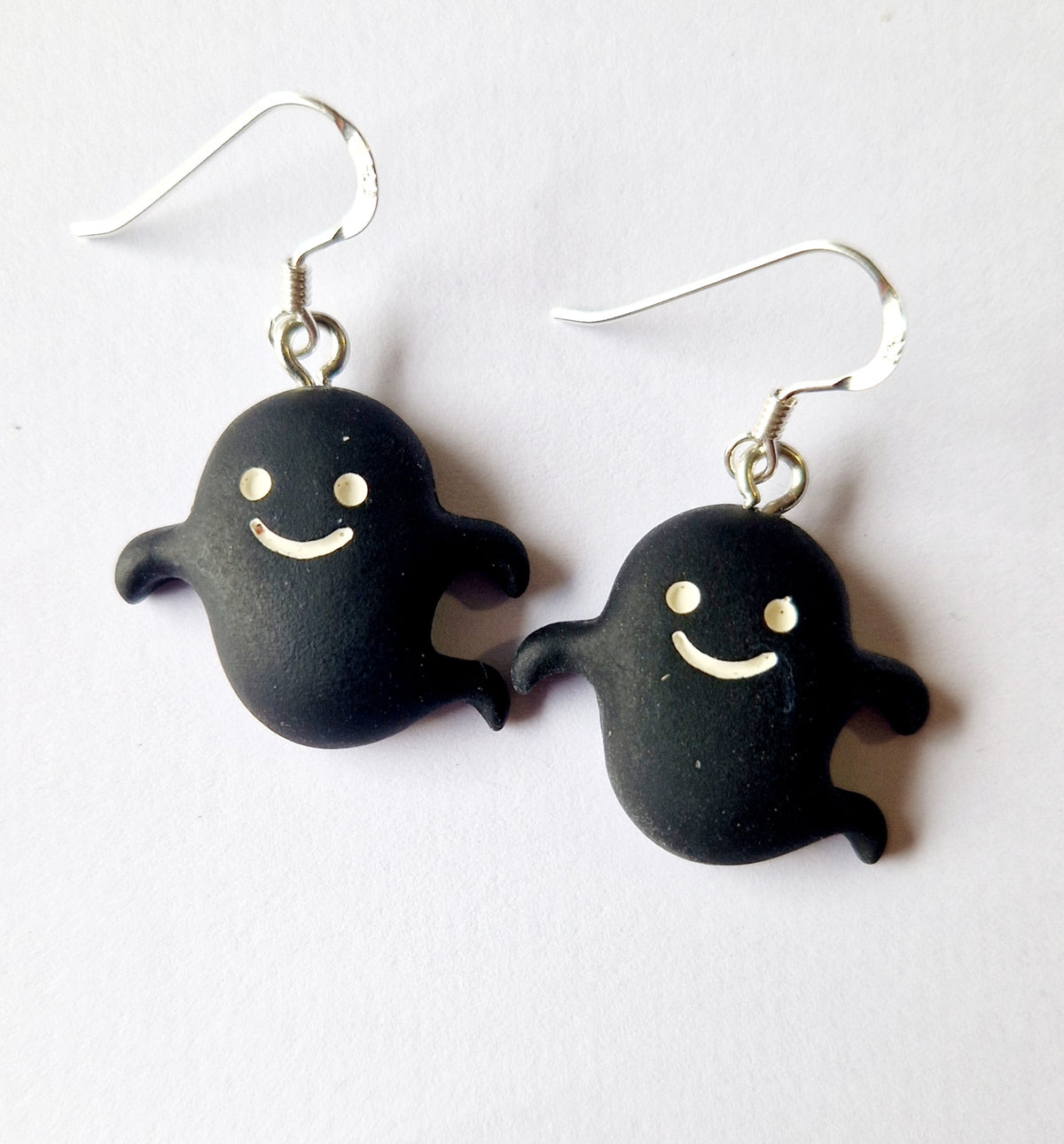 A pair of black ghost-shaped dangle earrings with sterling silver fishhook wires and small white facial details, shown on a plain light background.