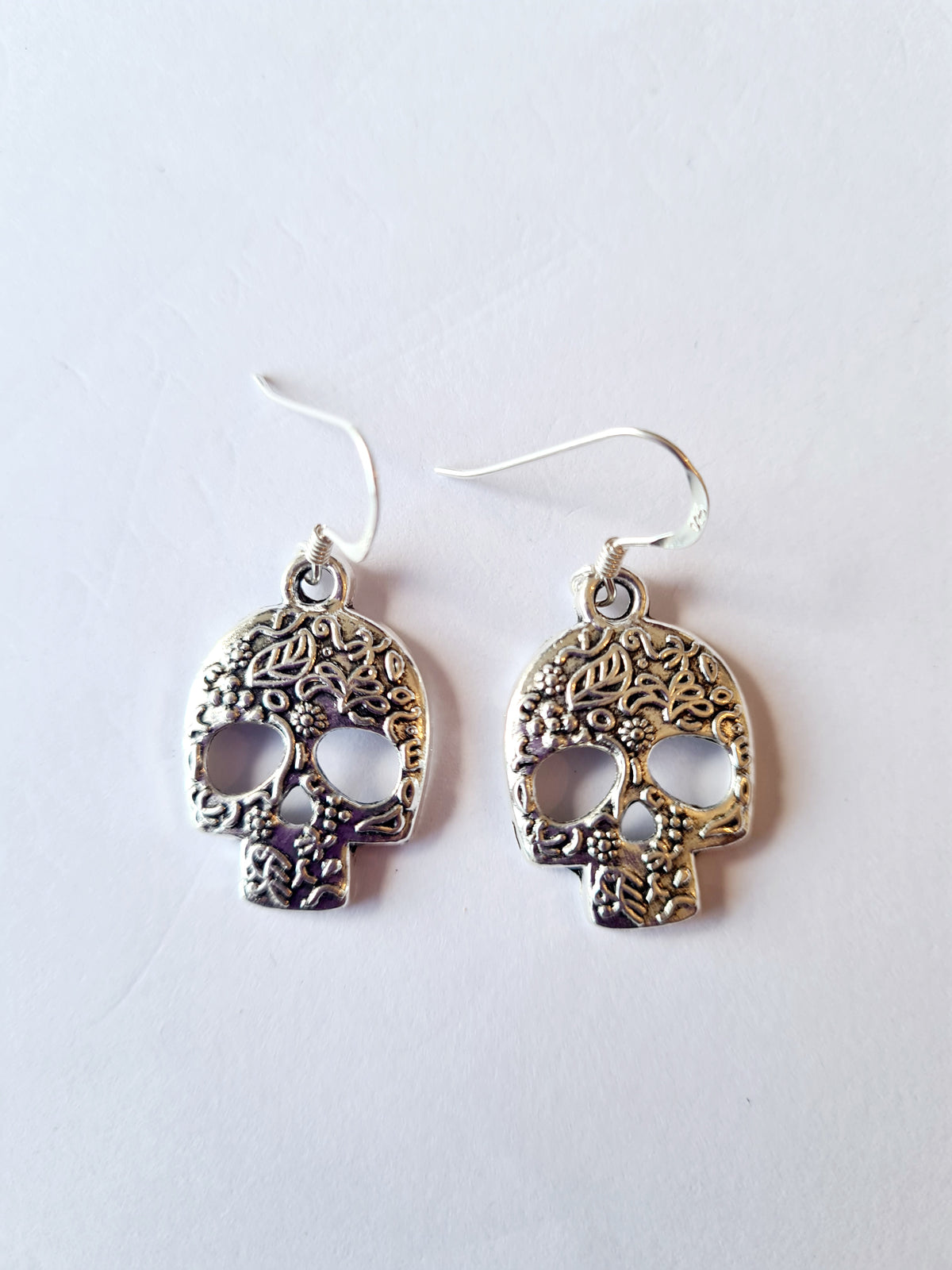 A pair of silver-toned skull dangle earrings on sterling silver with intricate filigree detailing, shown on a plain white background.