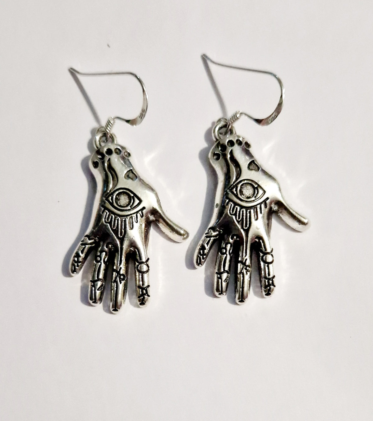 A pair of silver-toned Hamsa hand drop earrings with an all-seeing eye detail, shown on a plain white background.