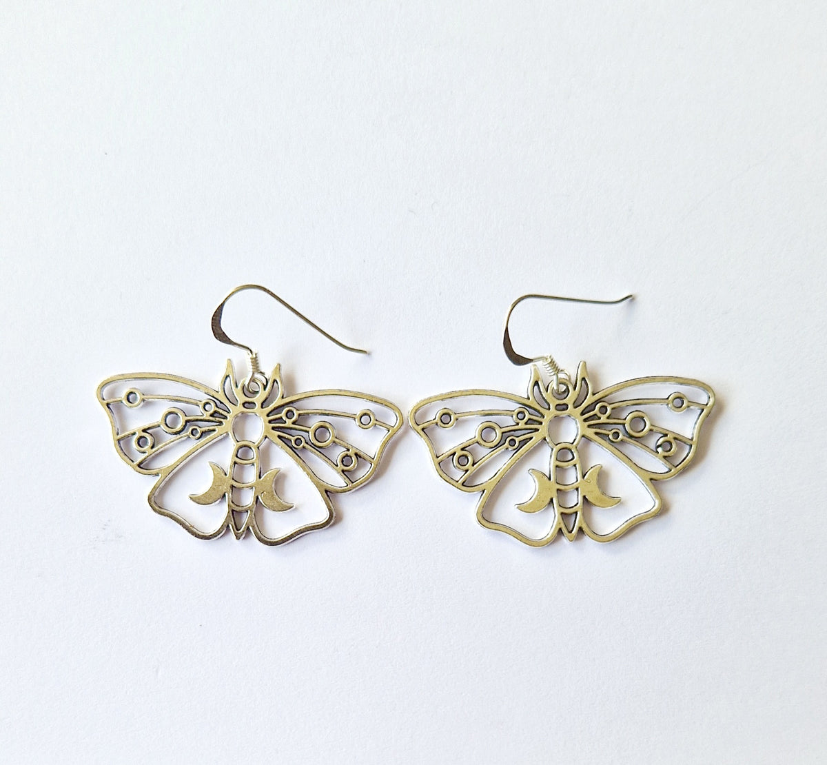 A pair of silver earrings shaped like moths with intricate cutout wing patterns and small circular details, displayed on a clean white background.