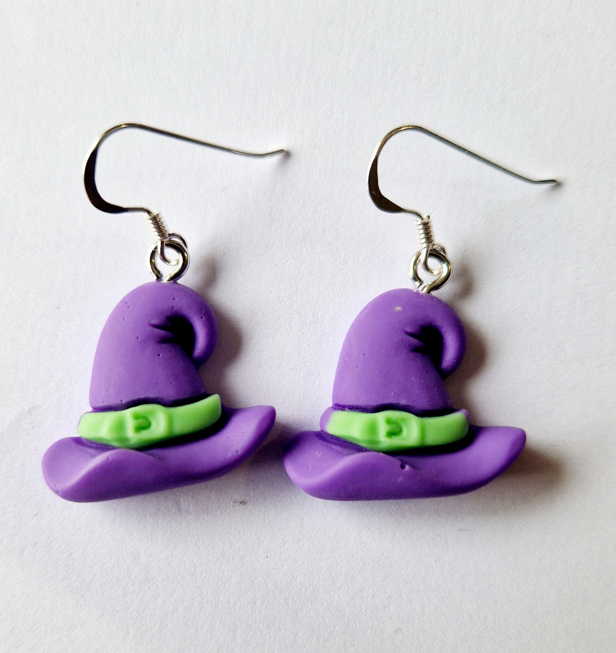 A pair of dangle earrings shaped like purple witch hats with lime green bands, suspended from sterling silver fishhook wires on a plain white background.