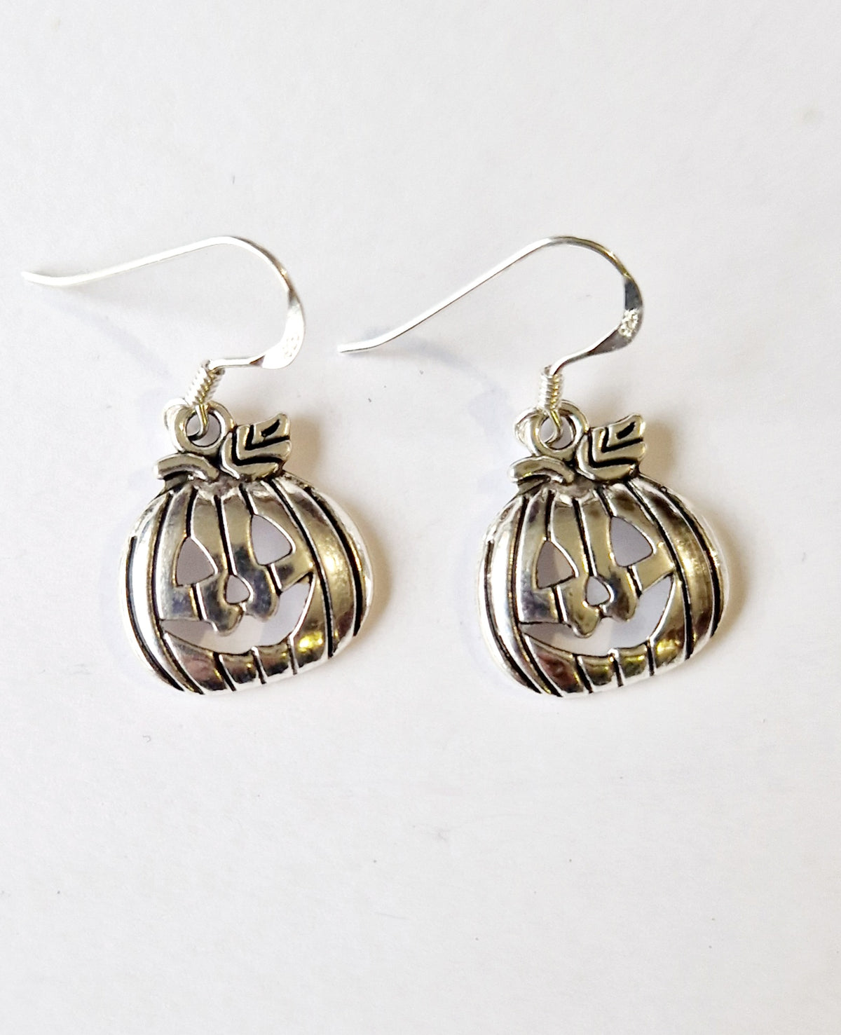 A pair of silver-toned dangle earrings shaped like carved jack-o'-lantern pumpkins, shown on a plain white background.