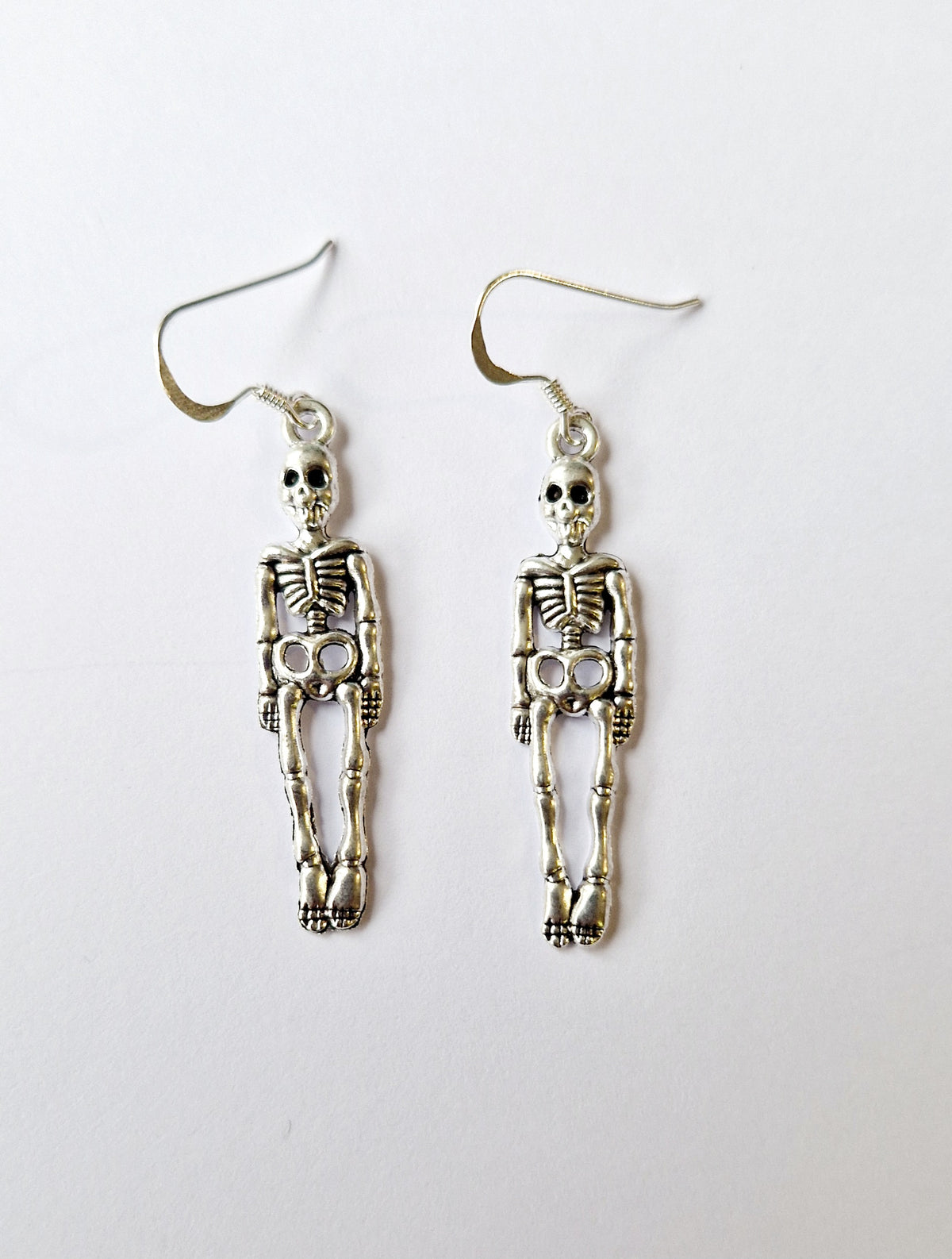 A pair of silver skeleton drop earrings with detailed articulated bones and sterling silver fishhook wires, displayed on a plain white background.