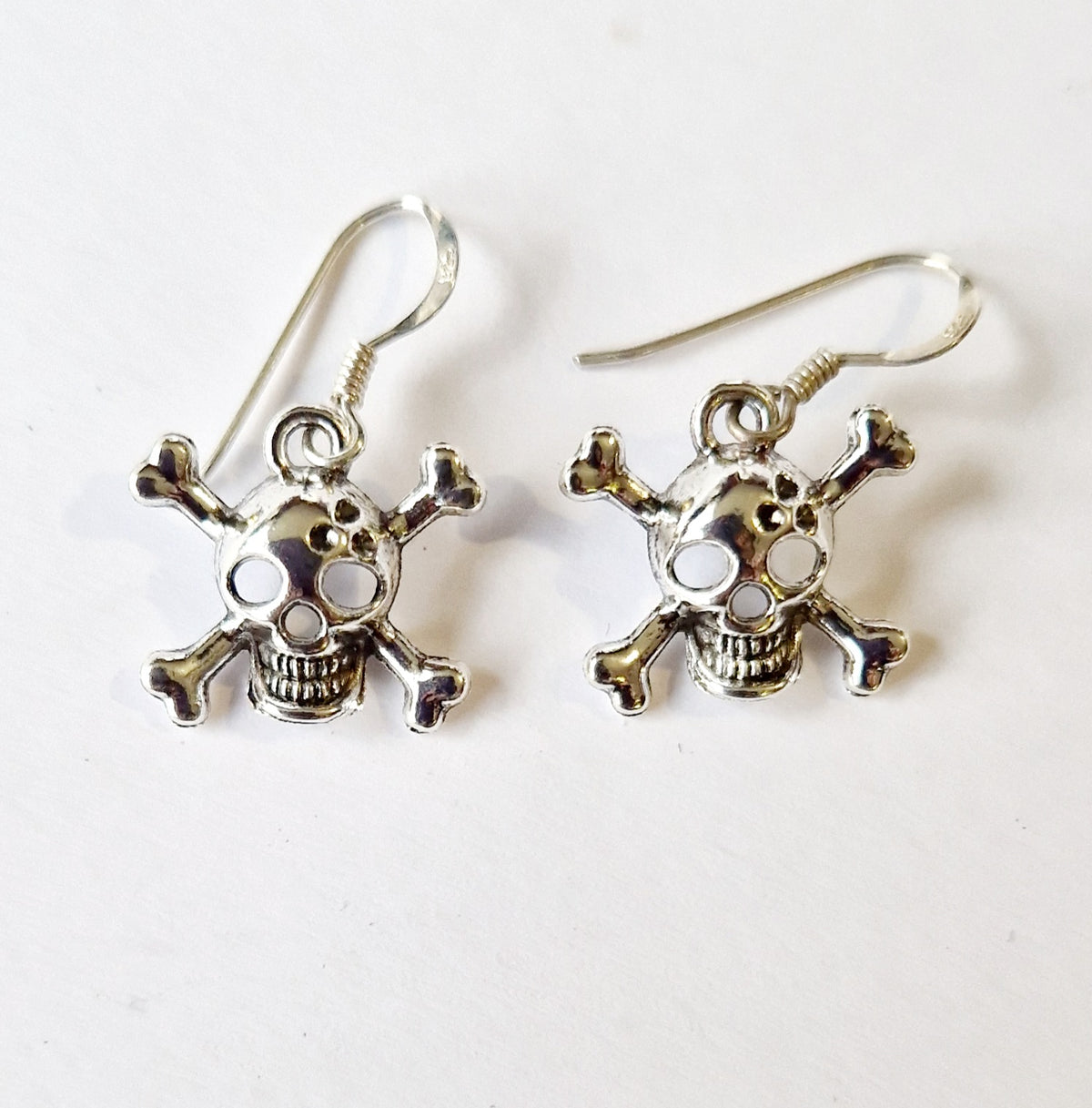 A pair of silver-toned skull and crossbones dangle earrings on a plain white background.