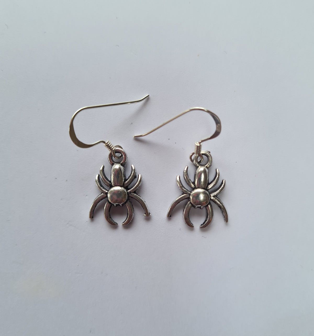 A pair of silver-toned spider dangle earrings on a plain white background.