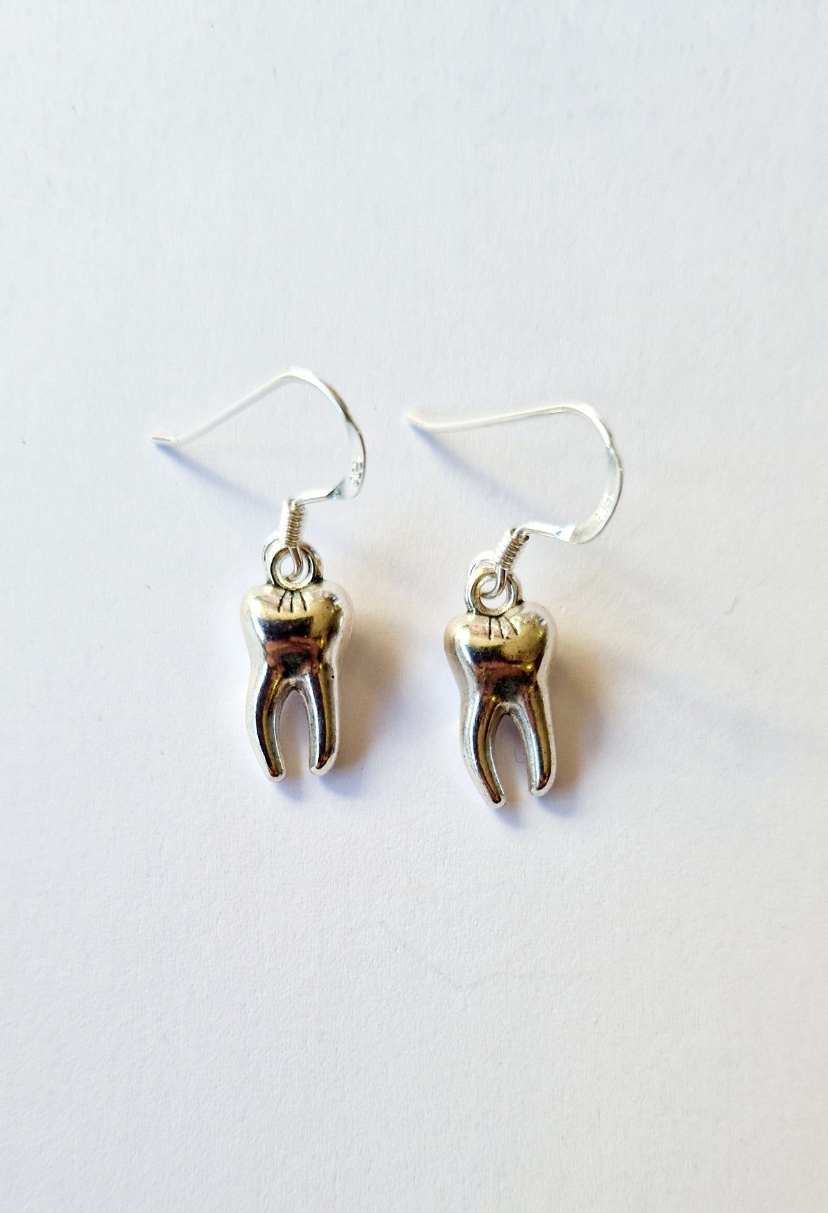 A pair of silver-toned teeth dangle earrings on a plain white background.