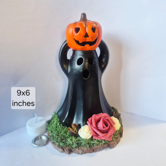 A handmade Candle and cone burner decor piece with an orange jack-o'-lantern on its head, black ghost body, faux moss base, decorative roses, and a small white tea light candle beside it. Text on the image reads 9x6 inches.