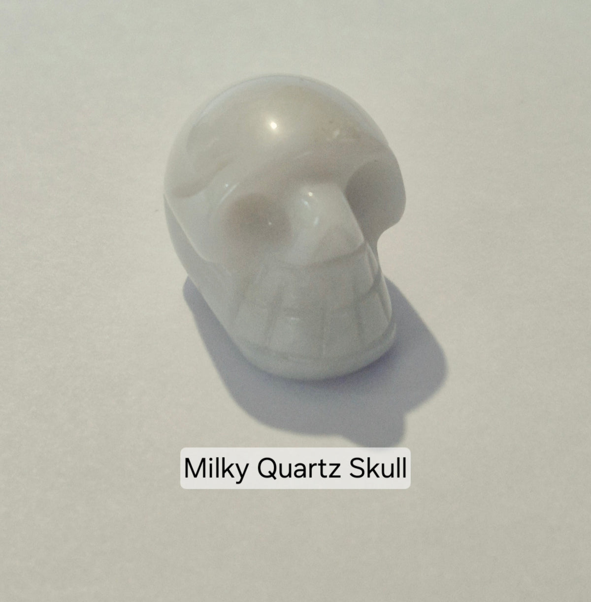 A small carved skull-shaped object made of milky translucent quartz, shown on a plain light background with the text 'Milky Quartz Skull' below it.