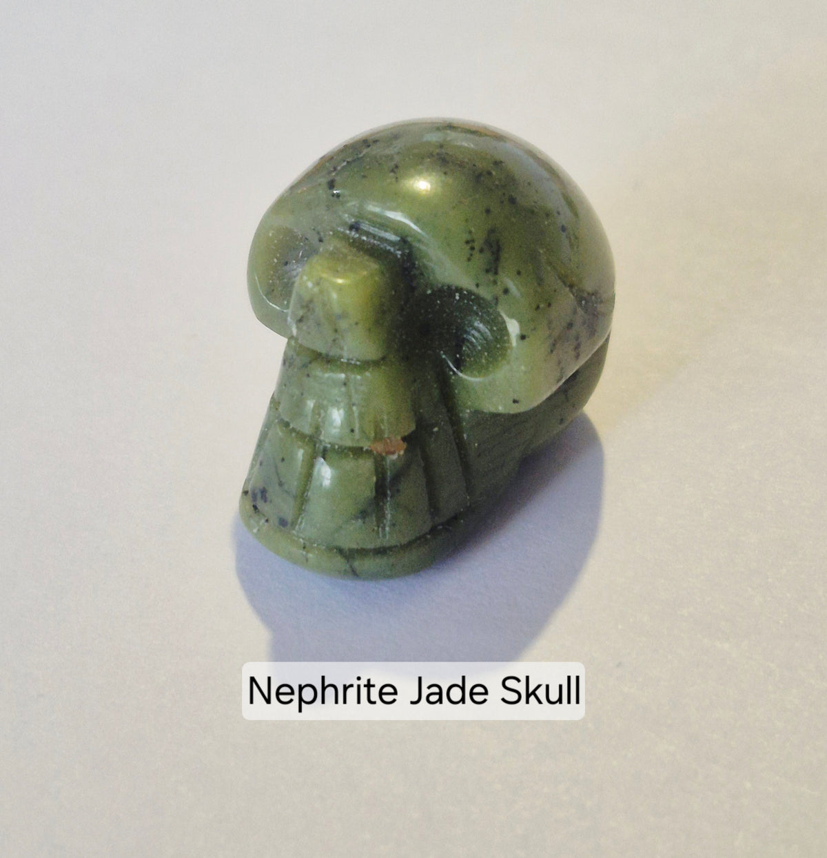 A small carved nephrite jade skull on a light gray background with a text label underneath reading 'Nephrite Jade Skull'.