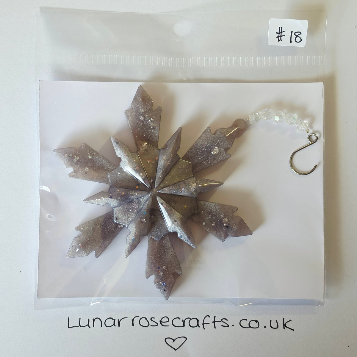A packaged snowflake ornament with a faceted metallic silver and gray design, small clear glittery tones, and a silver hook at the top, sealed in a clear plastic bag on a white backing card. A handwritten label says #18, and Lunarrosecrafts.co.uk'