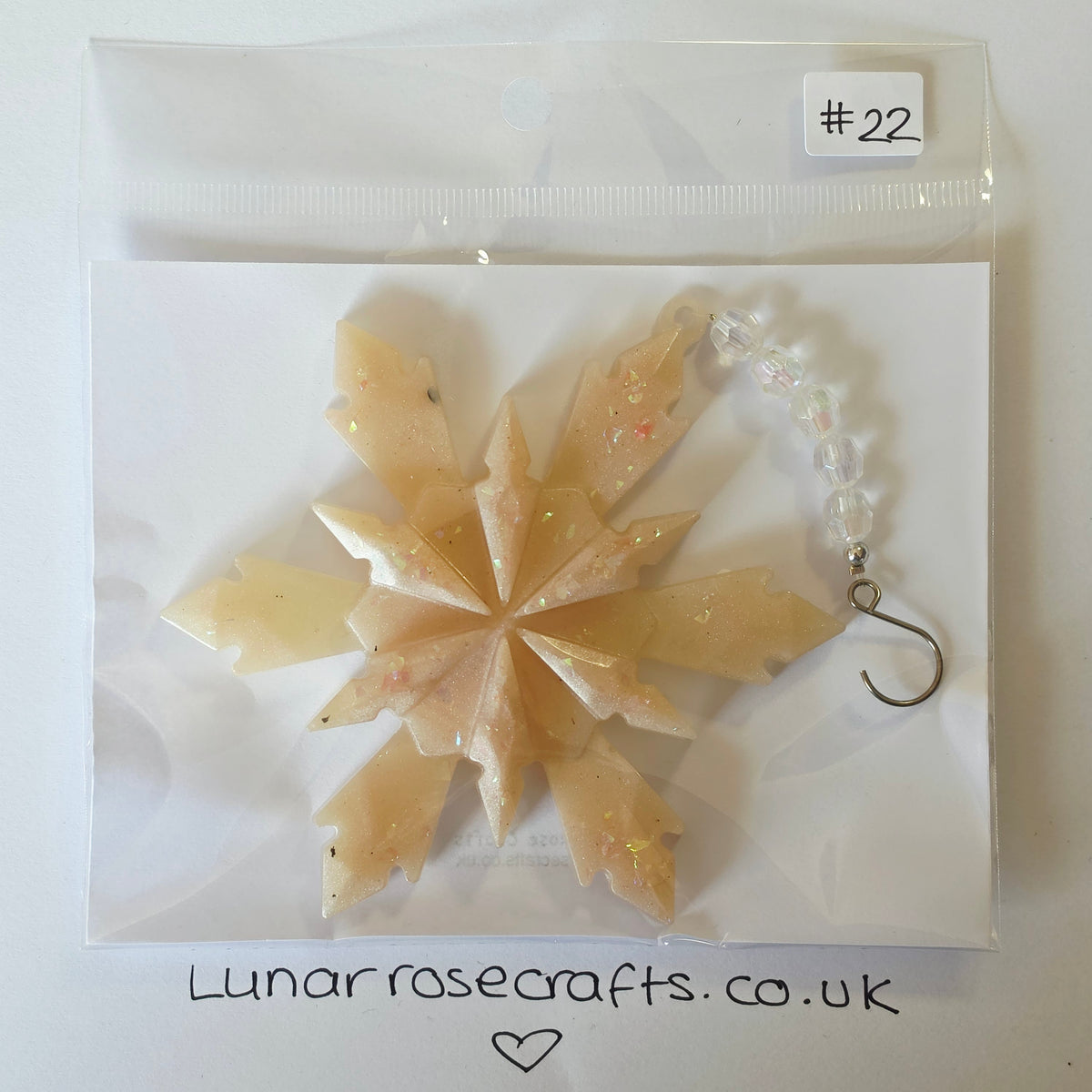 A handmade resin snowflake ornament in a pale peach-beige color with embedded glitter, packaged in a clear plastic bag with a white backing card. A white label at the top right reads '#22', and the brand name 'Lunarrosecrafts.co.uk'