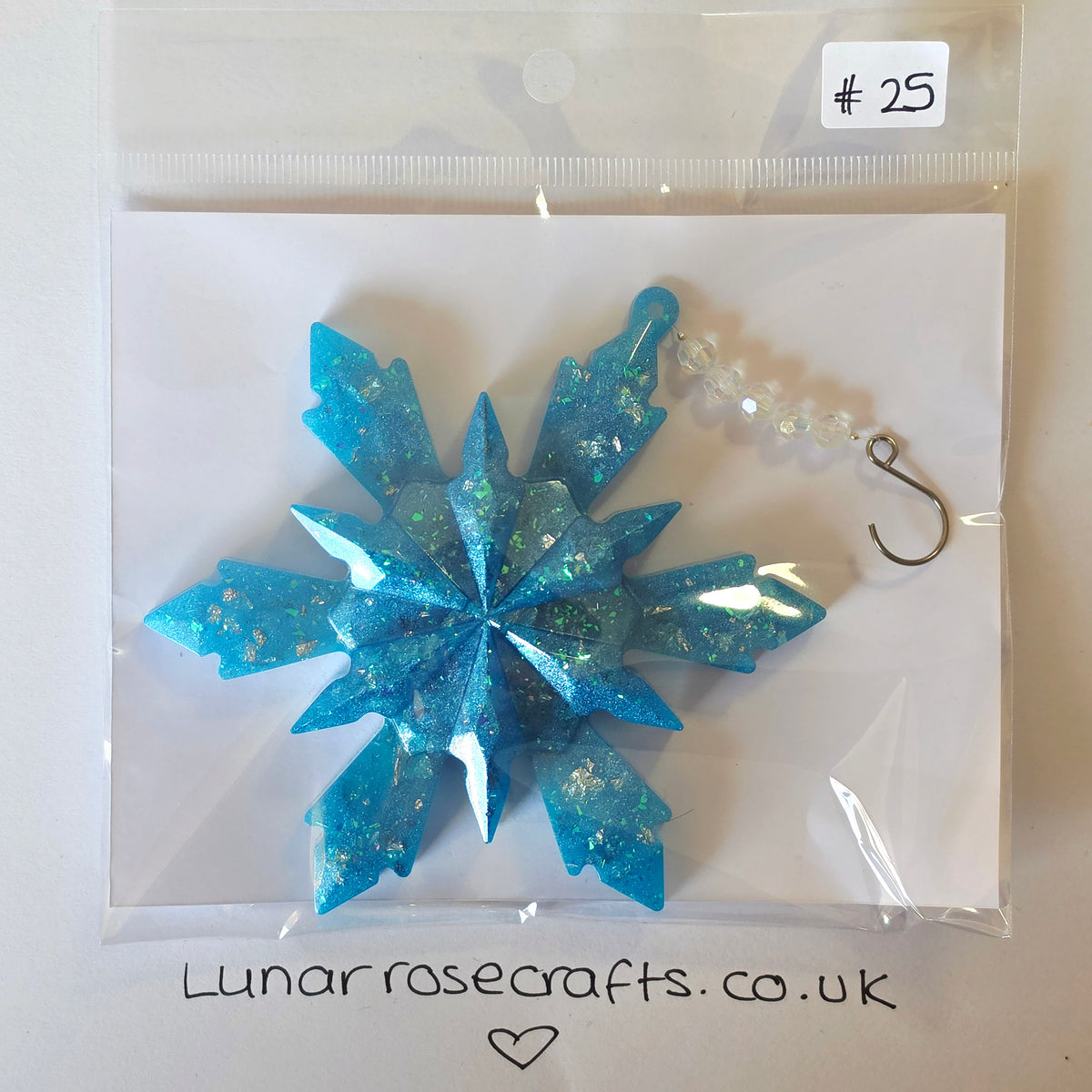 A blue glittery snowflake ornament with a clear beaded loop and metal hook, sealed in a clear plastic bag with a handwritten price tag and Lunarrosecrafts.co.uk
