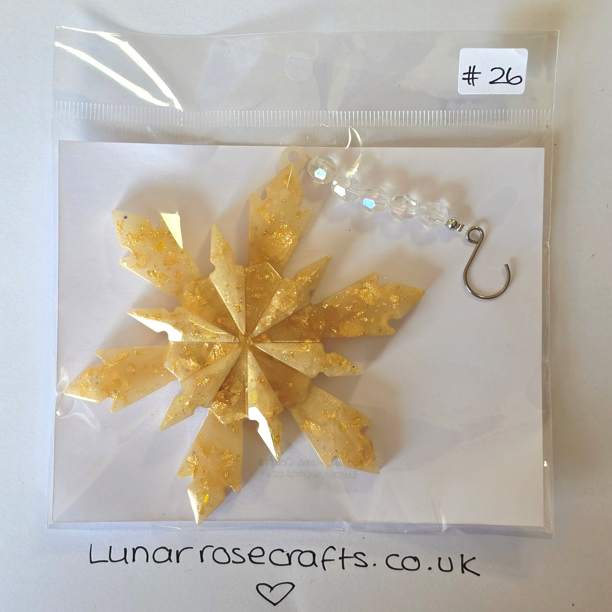 A packaged handmade gold glitter snowflake ornament with a beaded hook charm, sealed in a clear plastic bag with a handwritten price label '#26' and the website 'Lunarrosecrafts.co.uk'