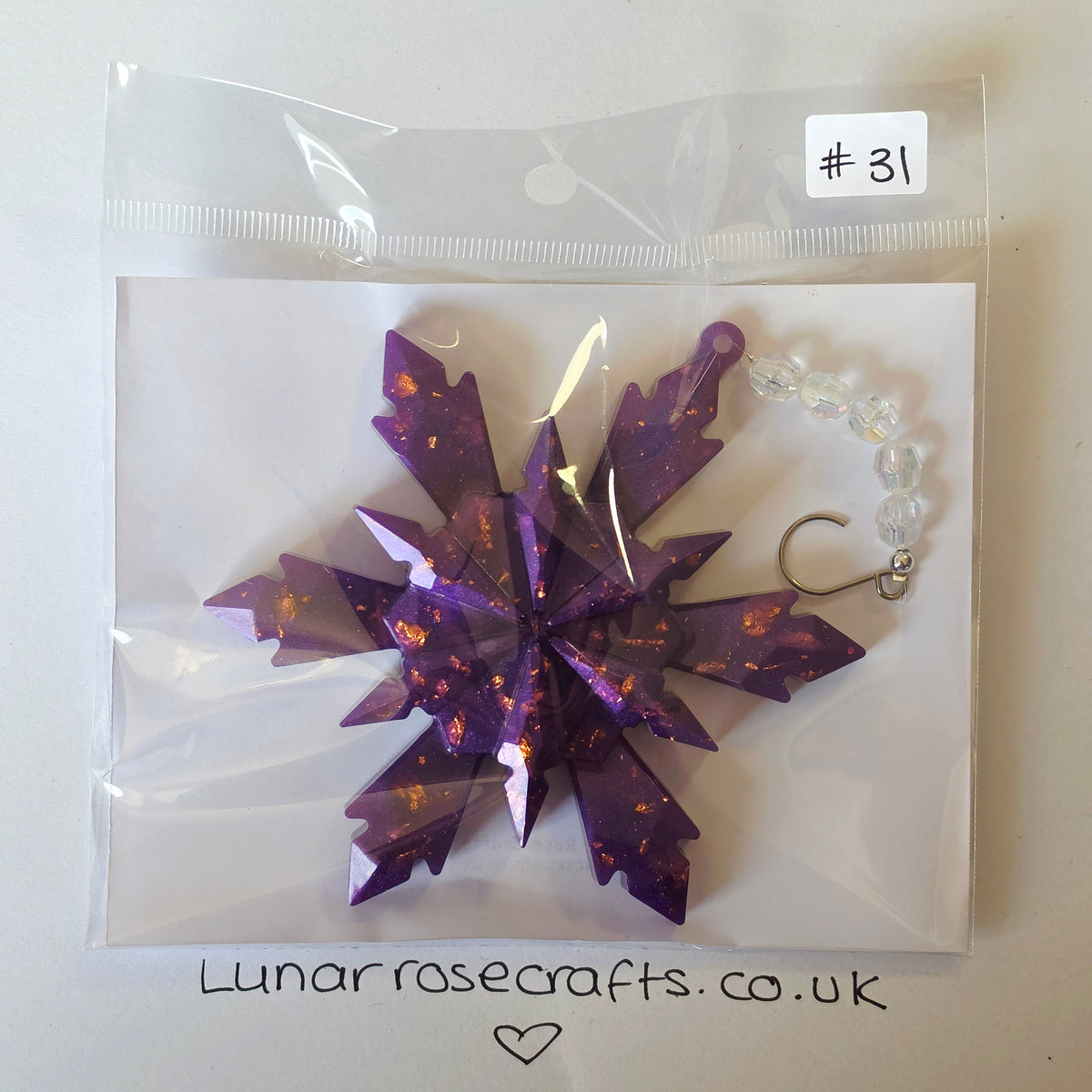 A purple glittery snowflake-shaped ornament with a silver fishhook and clear beaded loop, sealed in a clear plastic bag with a handwritten label '#31' and 'Lunarrosecrafts.co.uk'