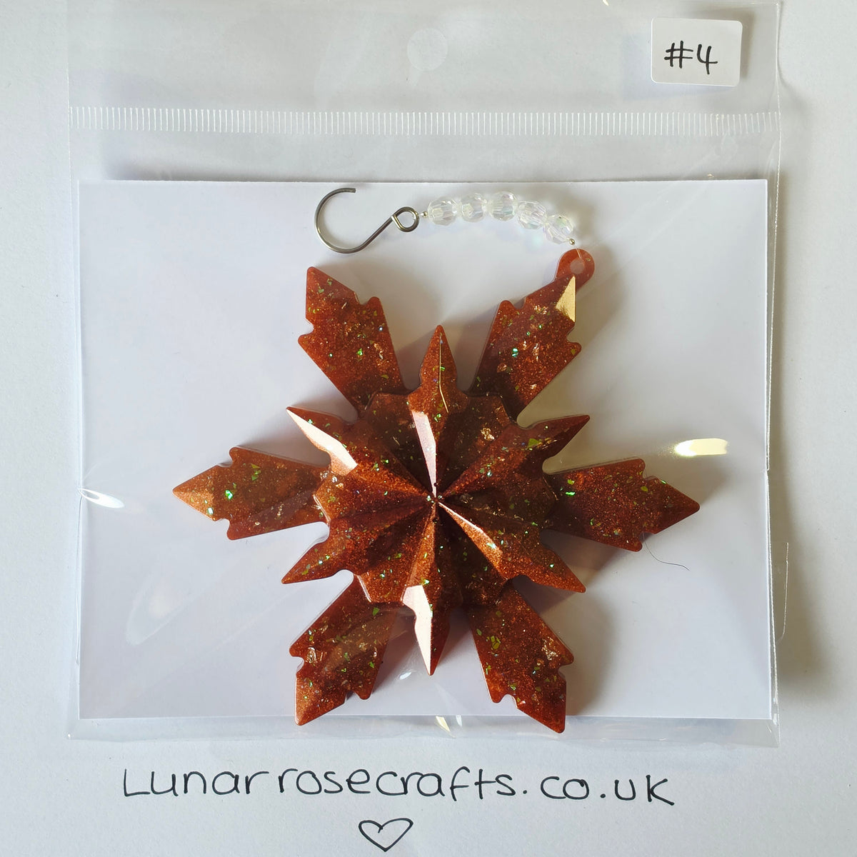 A glittery copper-red snowflake ornament with a silver hook and clear beads, packaged in a clear plastic bag on a white backing card.