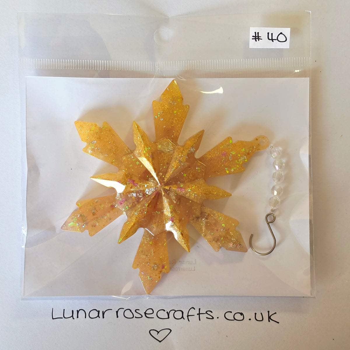 A glittery gold snowflake ornament with embedded rhinestones, packaged in a clear plastic bag with a white backing card. A small white label at the top right reads '#40', and the bottom of the image shows 'Lunarrosecrafts.co.uk'