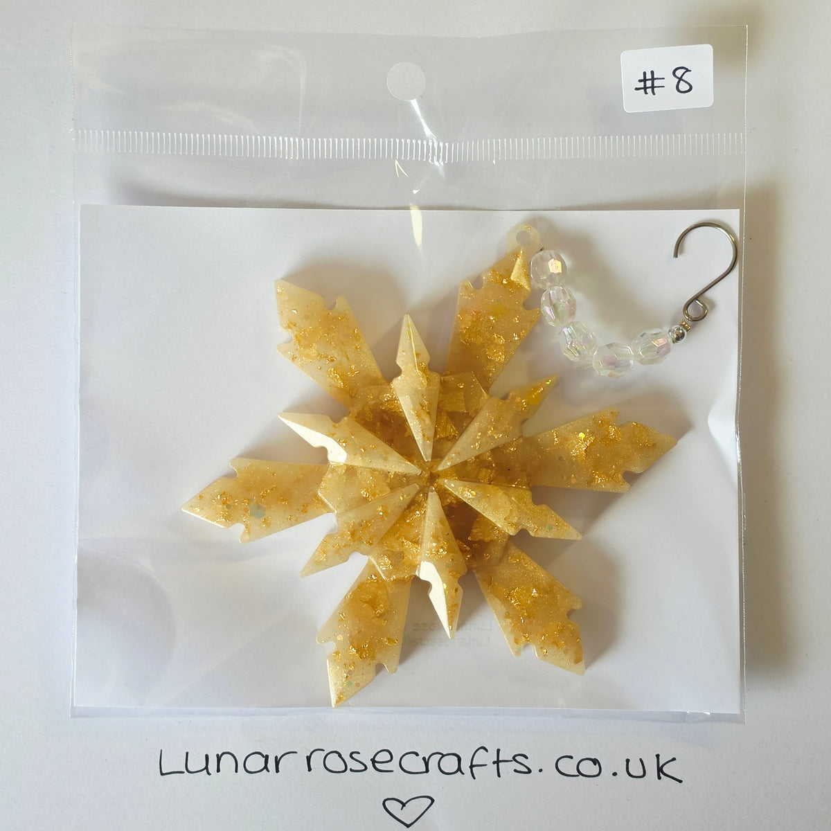 A gold glittery snowflake-shaped hangie with a clear beaded loop and silver hook clasp, displayed inside a clear plastic bag on a white backing card. A handwritten label says '#8' and the card shows 'Lunarrosecrafts.co.uk'