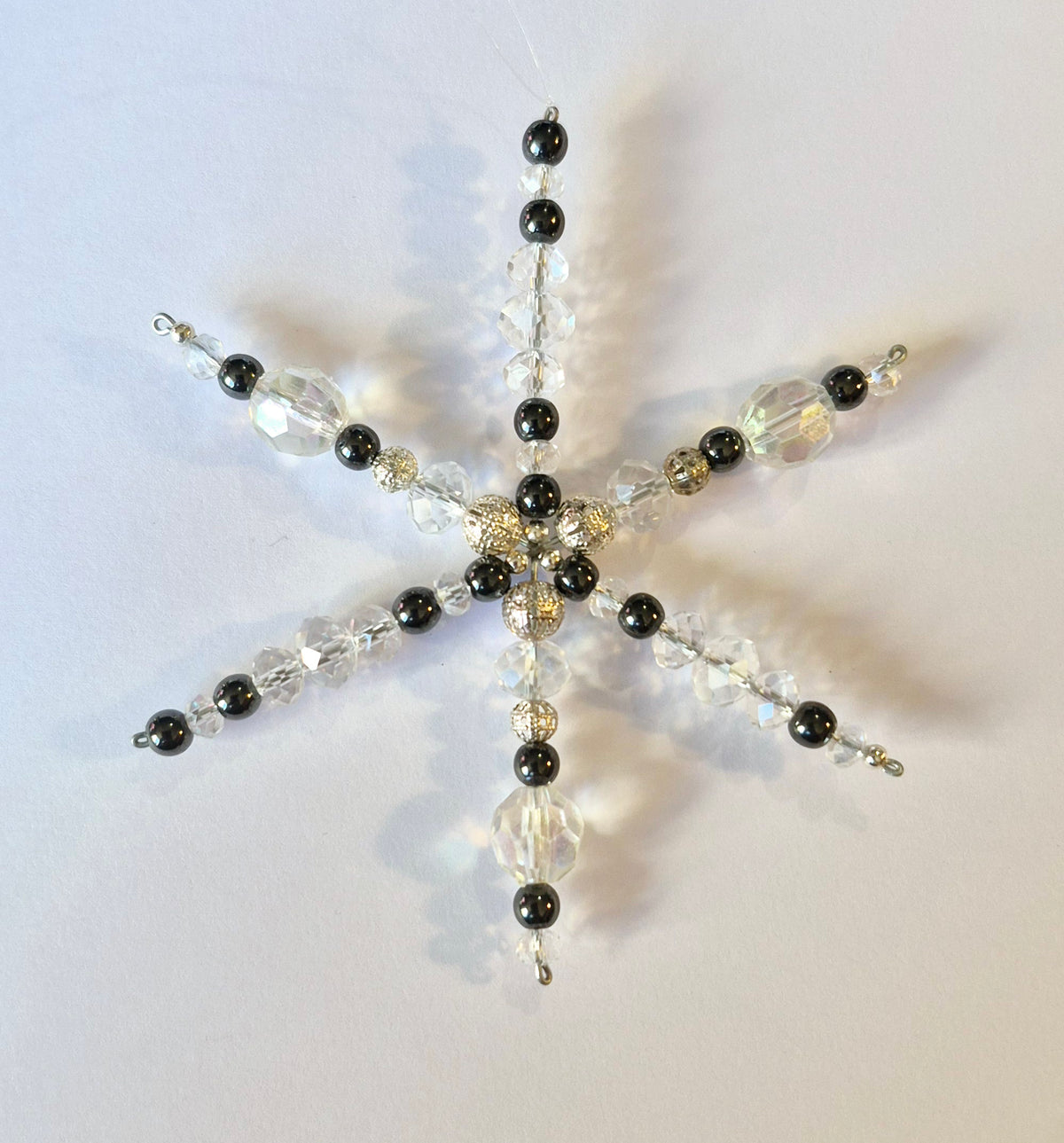 A six-pointed snowflake ornament made of black and clear faceted beads, displayed against a plain off-white background.