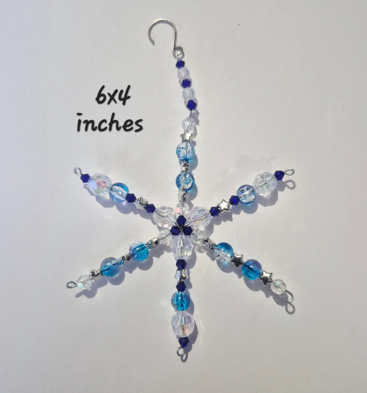 A snowflake-shaped beaded ornament with blue, clear, and dark blue beads on a silver wire frame, shown on a white background with '6x4 inches' text.
