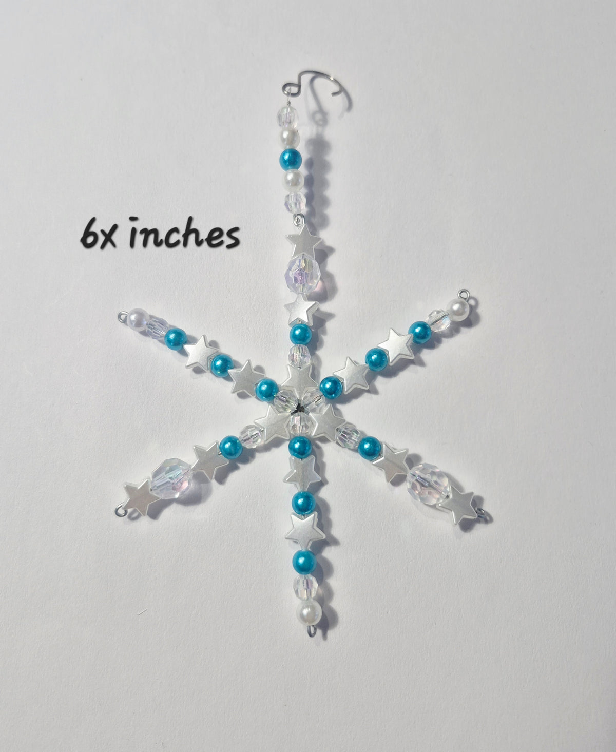 A snowflake-shaped Christmas ornament made of silver-toned metal, clear faceted beads, and bright blue beads, shown on a plain light background with the text '6x inches' printed to the left.