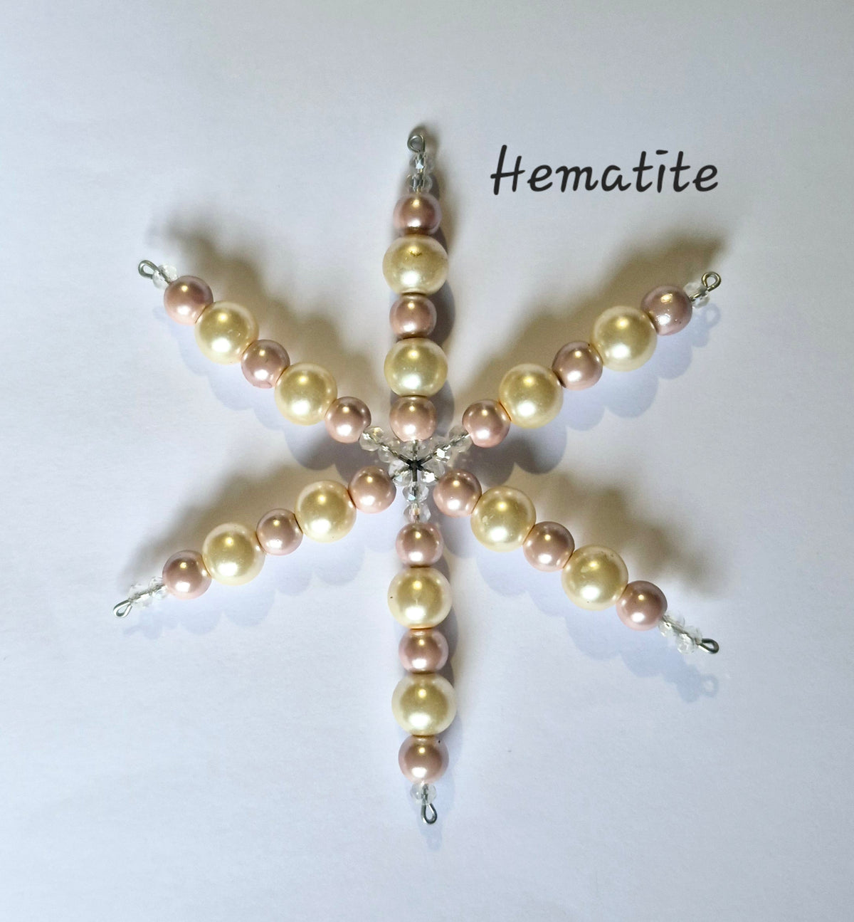 A handmade beaded star ornament made of pale gold and dusty rose pearls with silver-toned metal findings, displayed on a white background with the text 'Hematite' written above it.