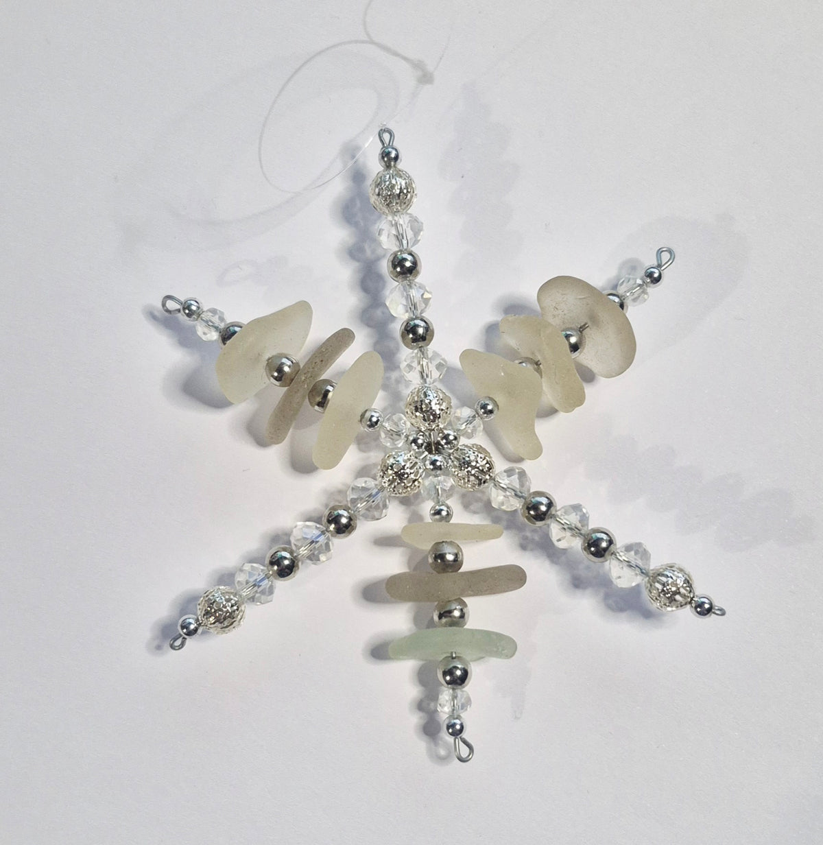 A handmade snowflake ornament made from sea glass and silver beads, displayed on a plain white background.