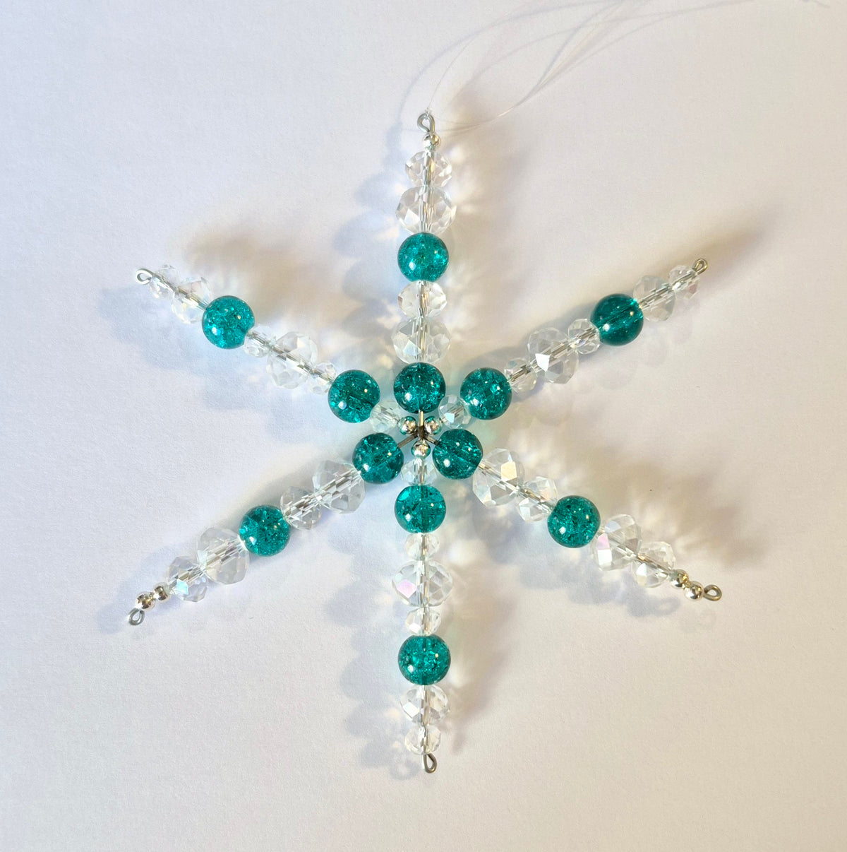 A handmade beaded snowflake ornament featuring glittery teal green beads and clear faceted crystal beads on a white background.