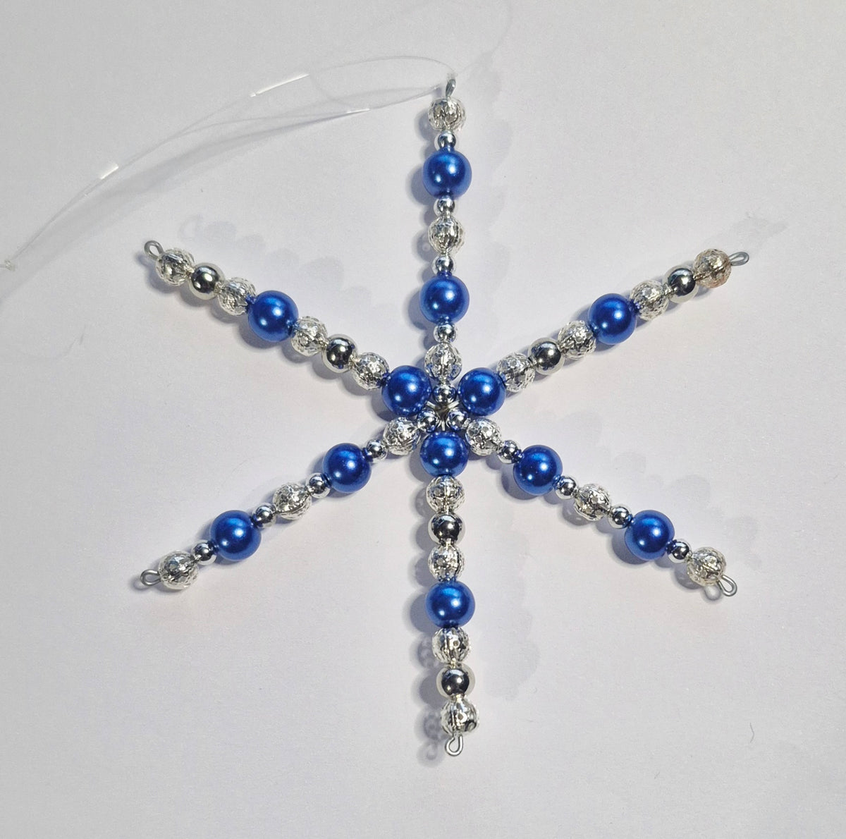 A snowflake-shaped Christmas ornament made of blue faux pearls and silver beads, shown on a plain light gray background.